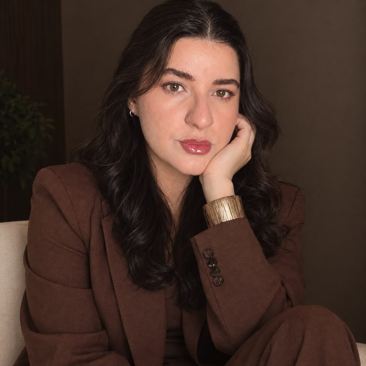 Mari Silva, micropigmentadora, de blazer café, com a mão apoiada no rosto